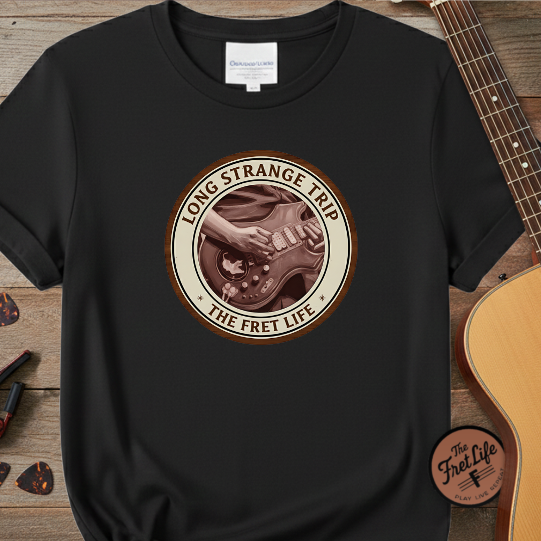 Black t-shirt with 'Long Strange Trip: The Fret Life' graphic on a wooden surface with a guitar.