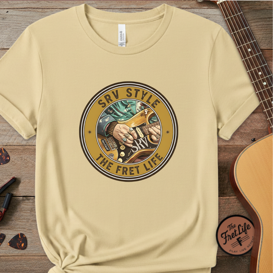 Beige t-shirt with guitar graphic and 'SRV Style The Fret Life' text on a wooden surface with a guitar.