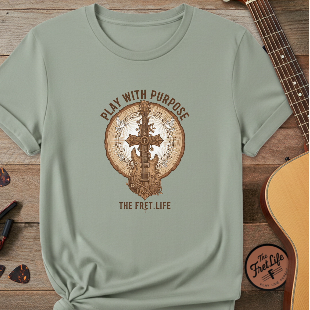 Sage green t-shirt with guitar graphic and text on a wooden surface with a guitar.