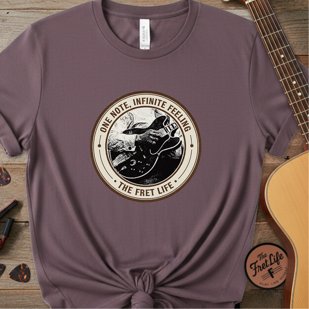 Purple t-shirt with a circular graphic and text on a wooden surface with a guitar.