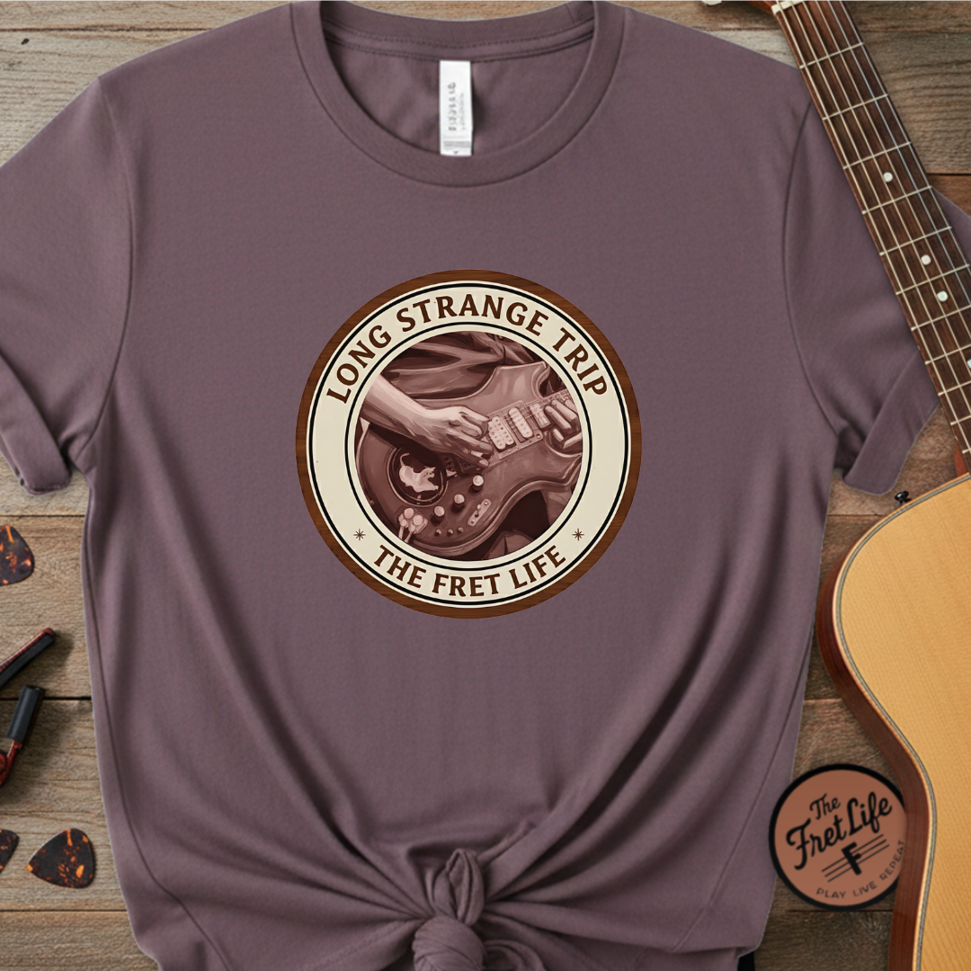 Purple t-shirt with 'Long Strange Trip: The Fret Life' graphic on a wooden surface with a guitar.