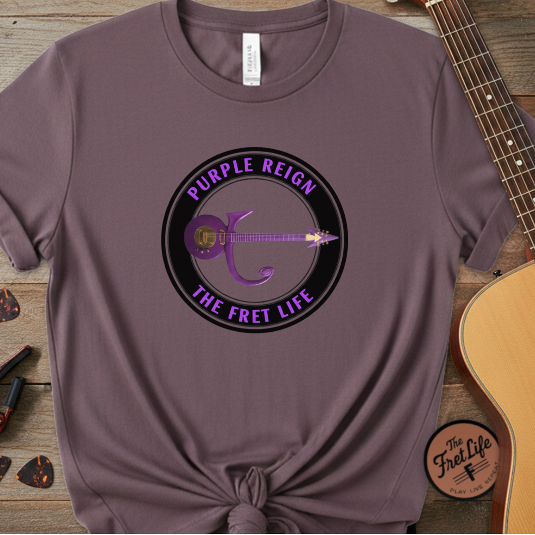 Purple t-shirt with 'Purple Reign, The Fret Life' design on a wooden surface with a guitar.