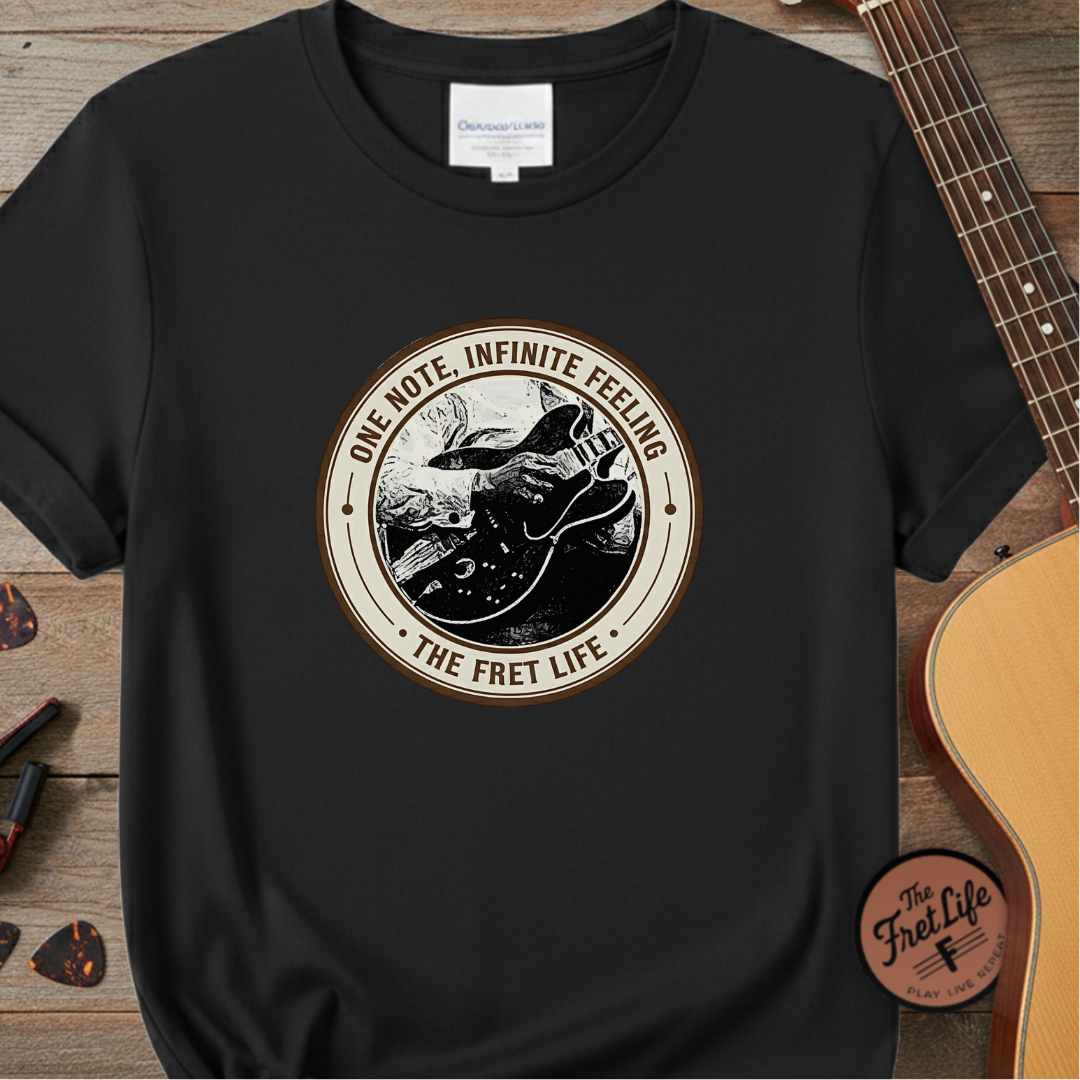 Black t-shirt with 'The Fret Life' graphic design on a wooden surface with a guitar.