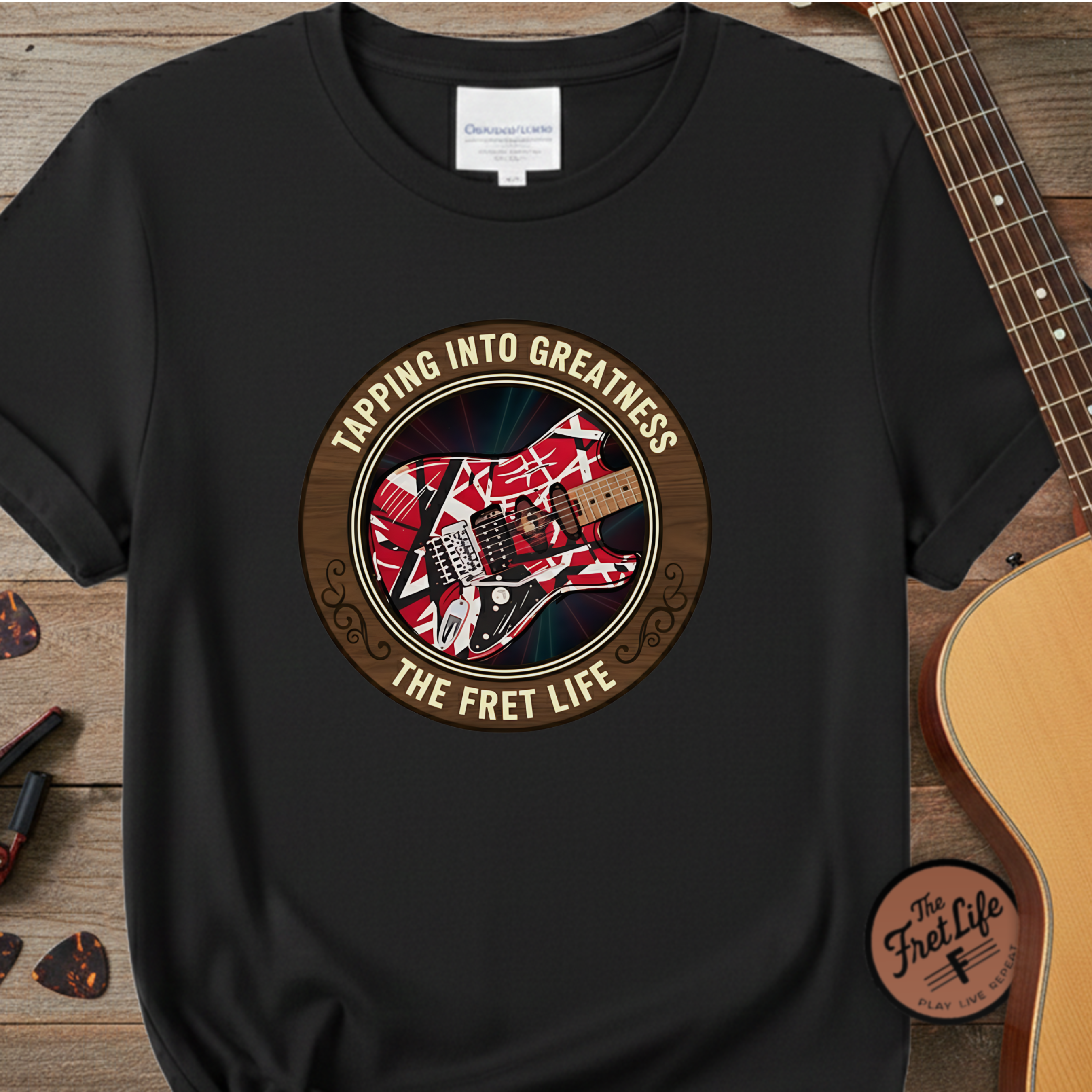 Black t-shirt with guitar graphic and text 'Tapping into Greatness: The Fret Life' on a wooden surface with a guitar.