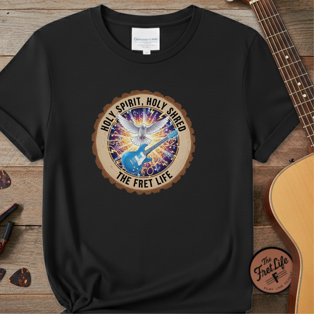 Black t-shirt with a colorful graphic and text on a wooden surface with a guitar.
