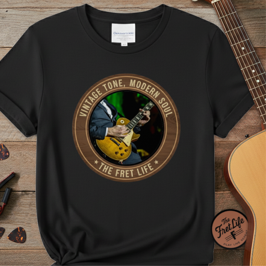 Black t-shirt with guitar graphic and text 'Vintage Tone, Modern Soul The Fret Life' on a wooden surface with a guitar.