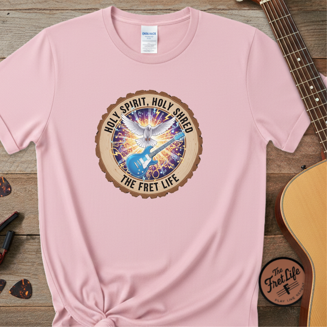 Pink t-shirt with a colorful graphic and text on a wooden surface with a guitar.