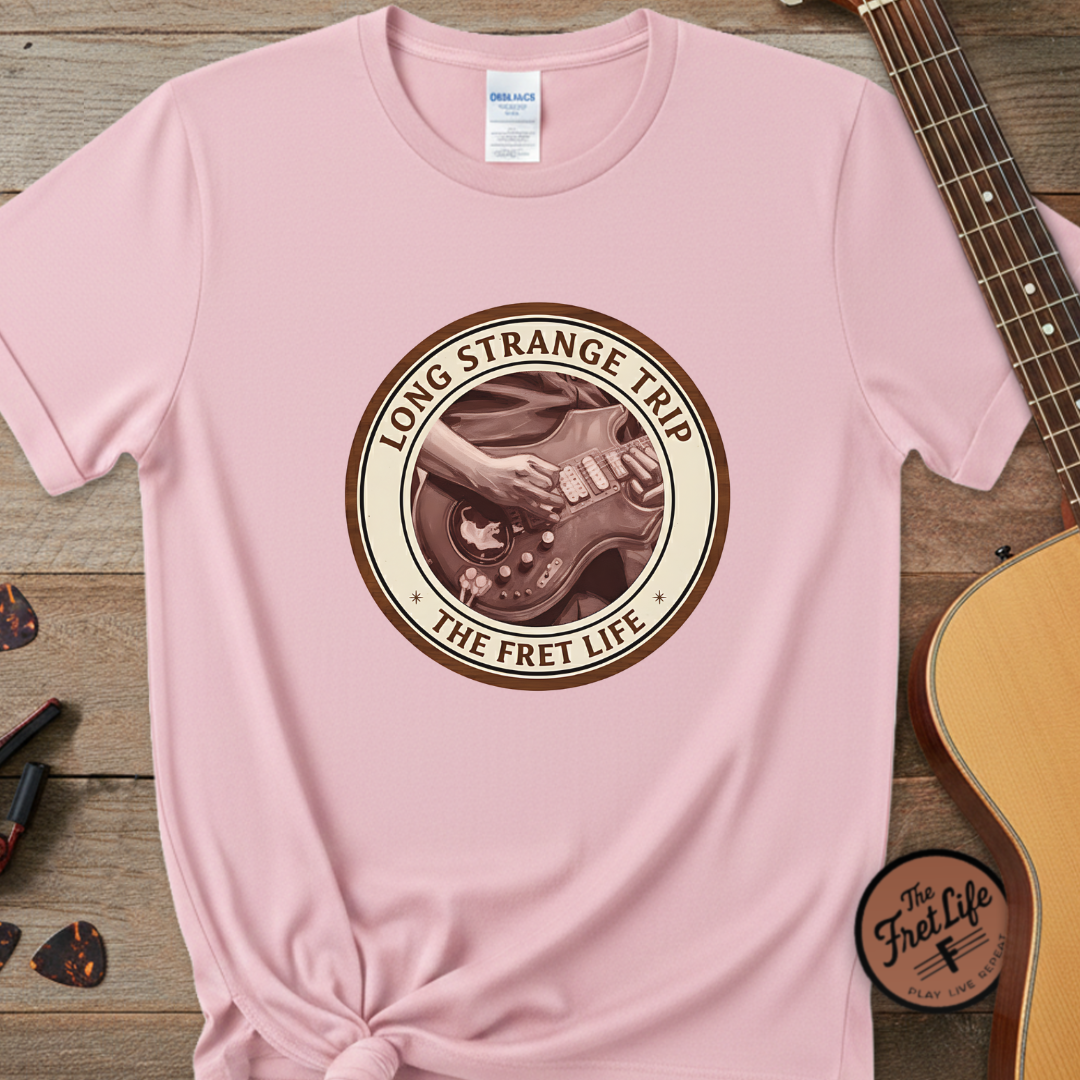 Pink t-shirt with 'Long Strange Trip' graphic design on a wooden surface with a guitar and pickguard.