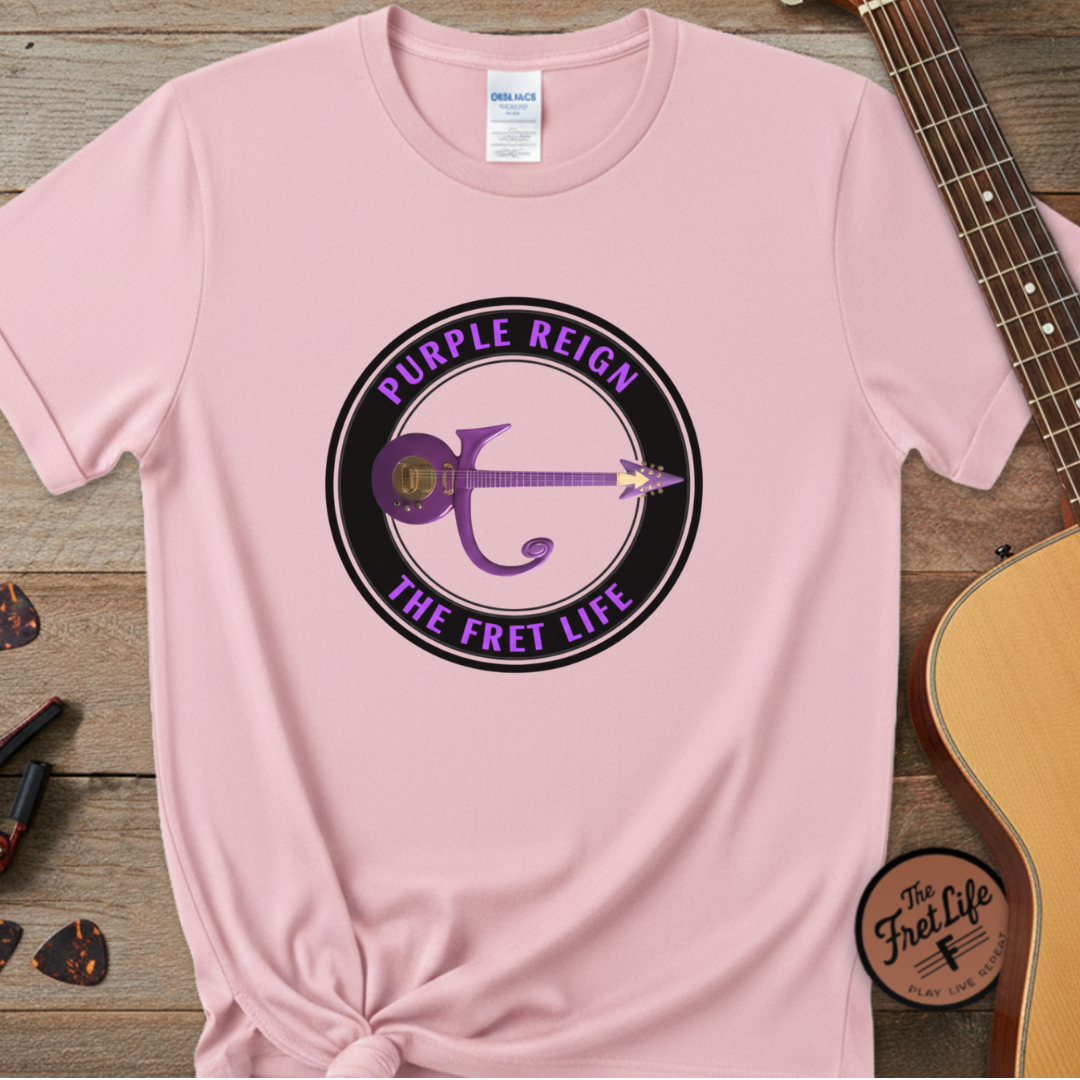 Pink t-shirt with 'Purple Reign The Fret Life' design on a wooden surface with a guitar.