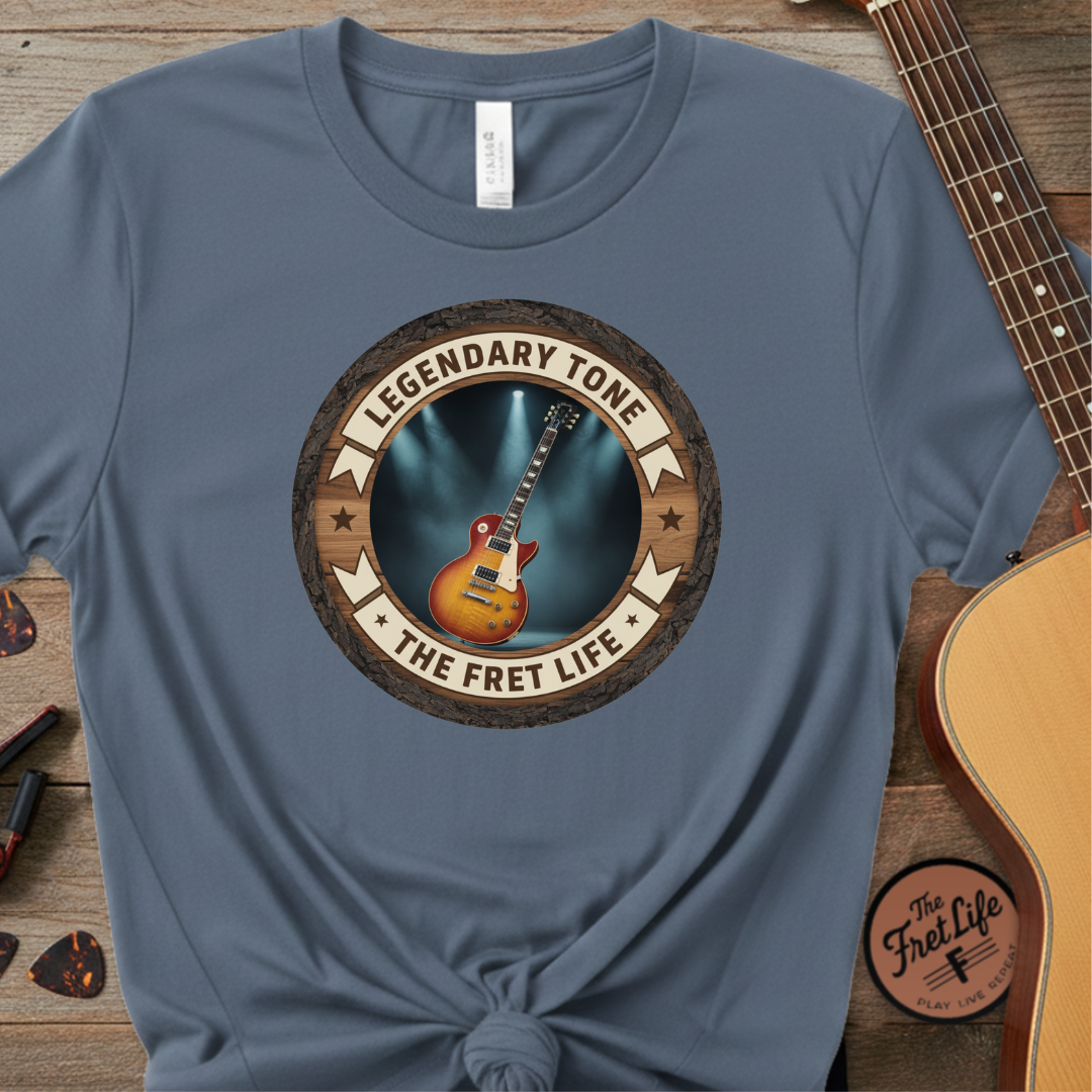 Blue t-shirt with guitar graphic and 'Legendary Tone The Fret Life' text on a wooden surface with a guitar.