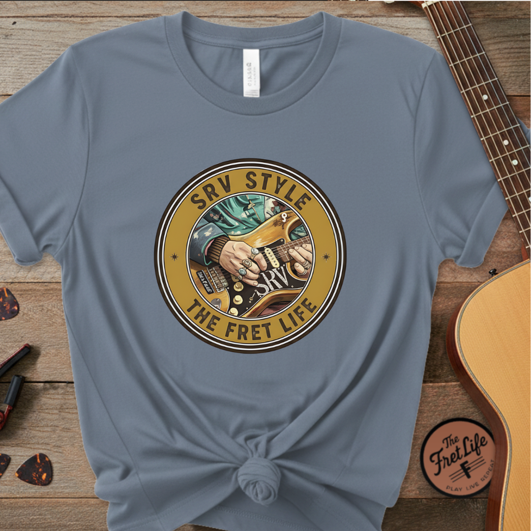 Blue t-shirt with a guitar-themed graphic and text on a wooden surface with a guitar.