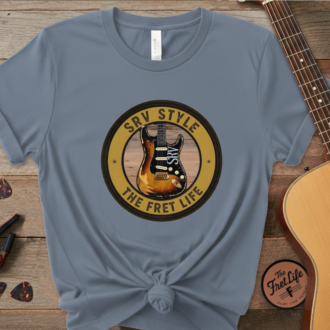 Blue t-shirt with guitar graphic and text on a wooden surface with guitars.