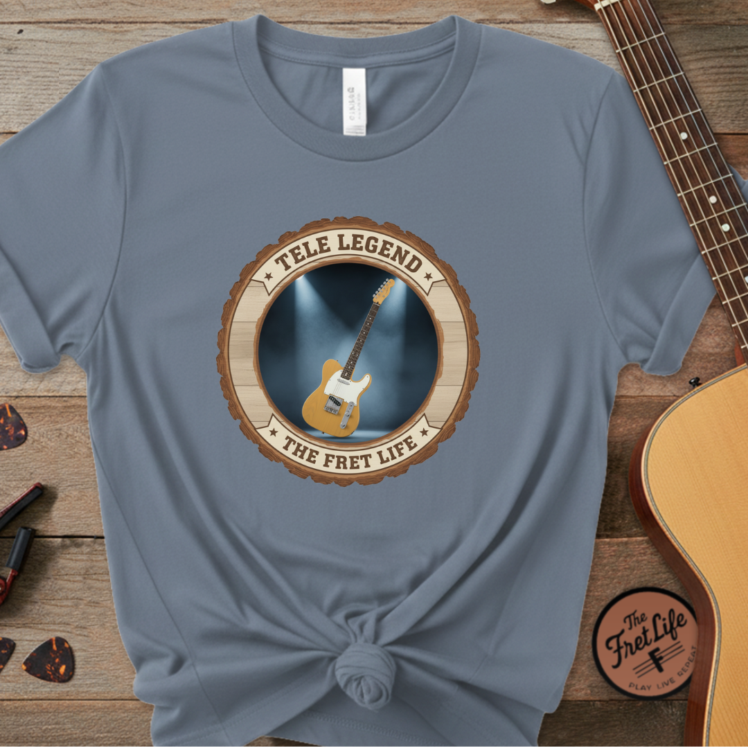 Blue t-shirt with guitar graphic and 'The Fret Life' text on a wooden surface with a guitar.