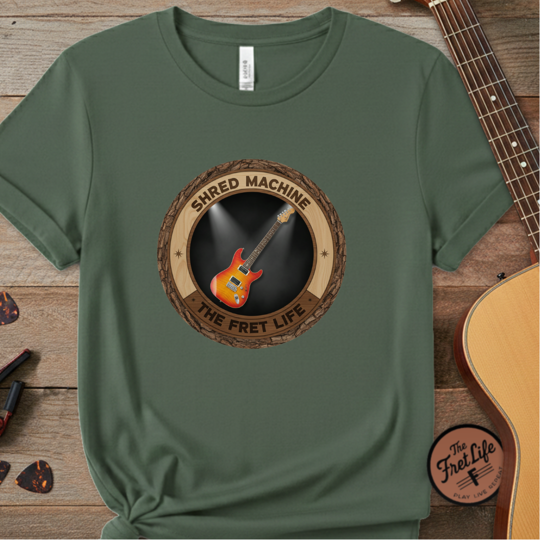 Green t-shirt with 'Shred Machine' graphic on a wooden surface with a guitar.