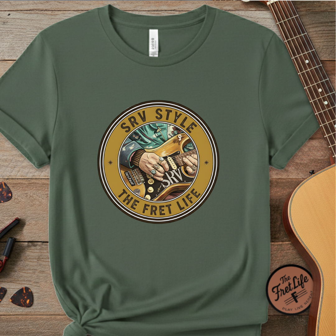 Green t-shirt with a guitar graphic and 'SRV Style The Fret Life' text on a wooden surface with a guitar.