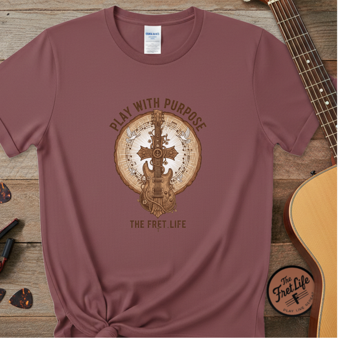 Maroon t-shirt with guitar graphic and 'Play with Purpose' text on a wooden surface with a guitar.