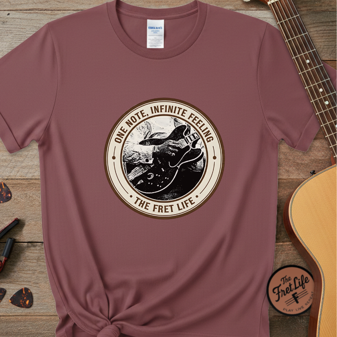 Maroon t-shirt with 'The Fret Life' graphic design on a wooden surface with a guitar.