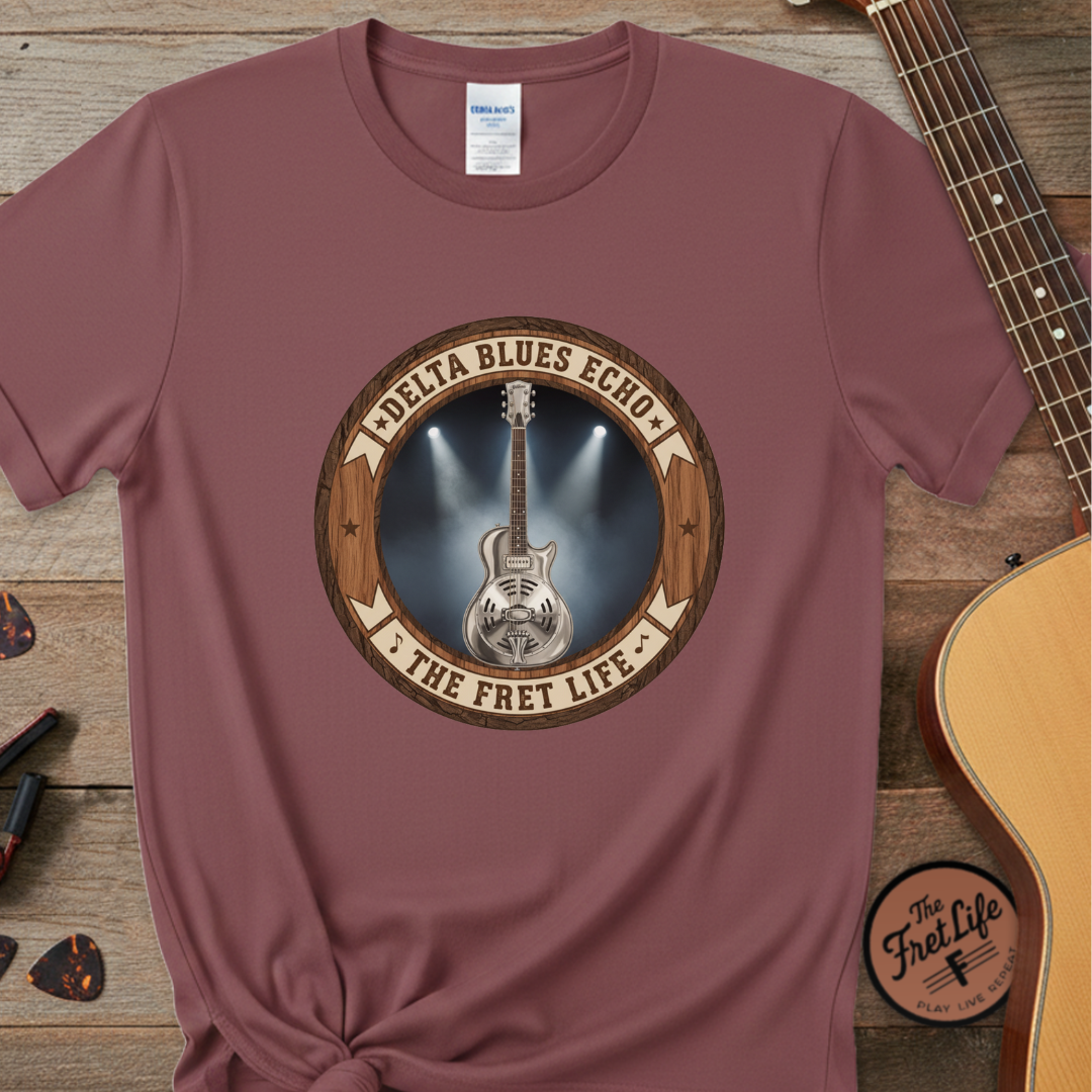 Maroon t-shirt with guitar graphic and text on a wooden surface with a guitar.
