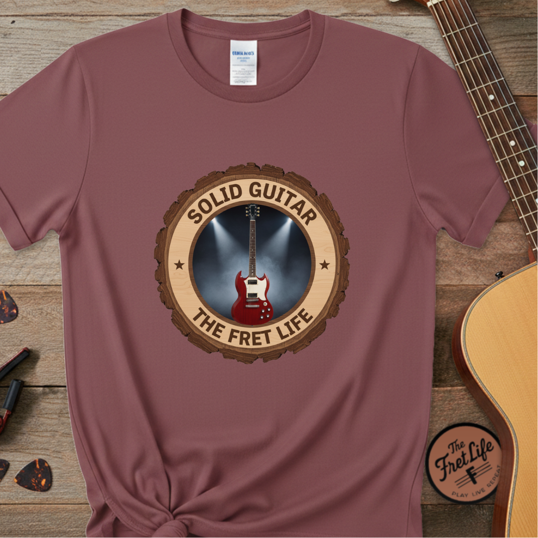 Maroon t-shirt with guitar graphic and 'Solid Guitar, The Fret Life' text on a wooden surface with a guitar.