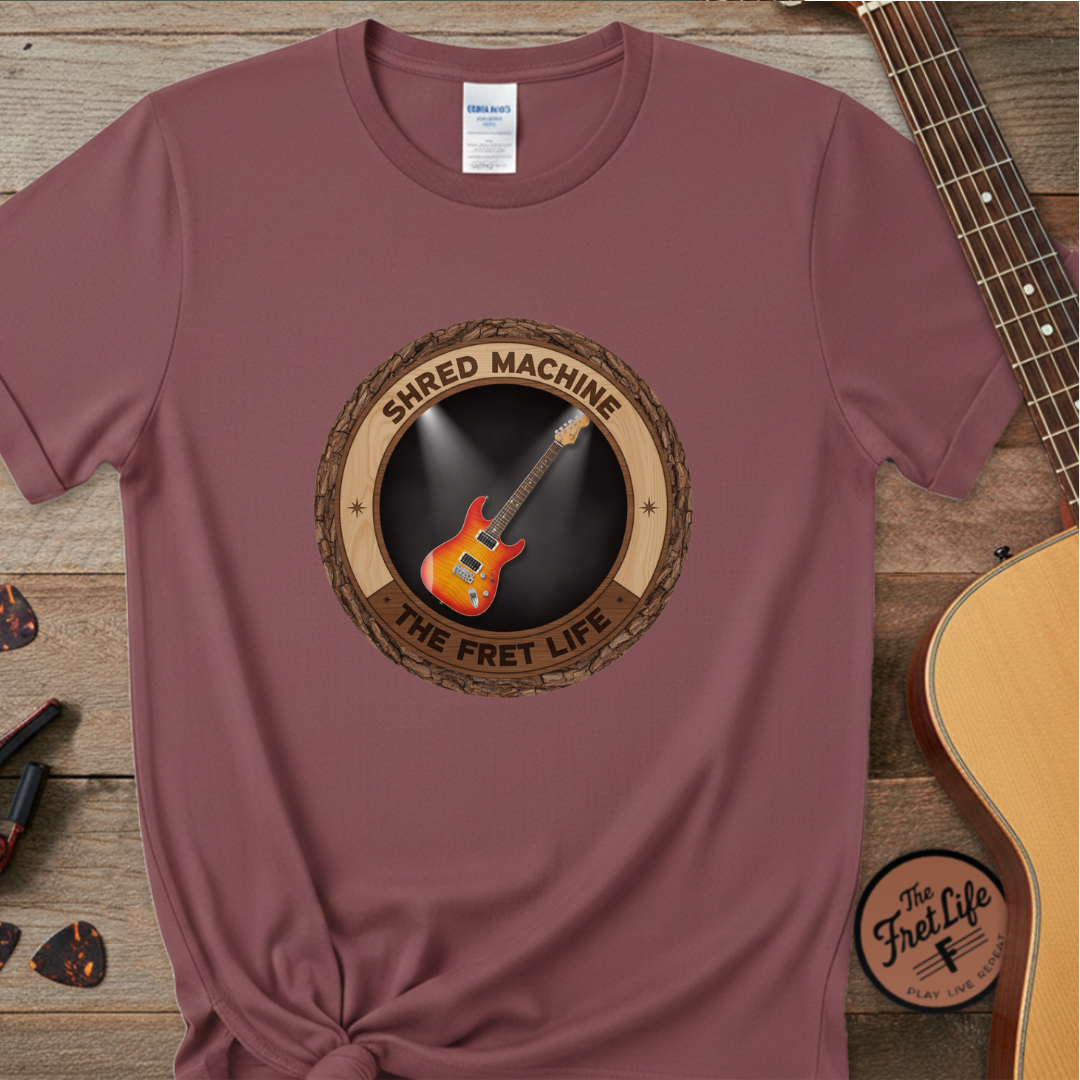 Maroon t-shirt with guitar graphic and 'Shred Machine' text on a wooden surface with a guitar.