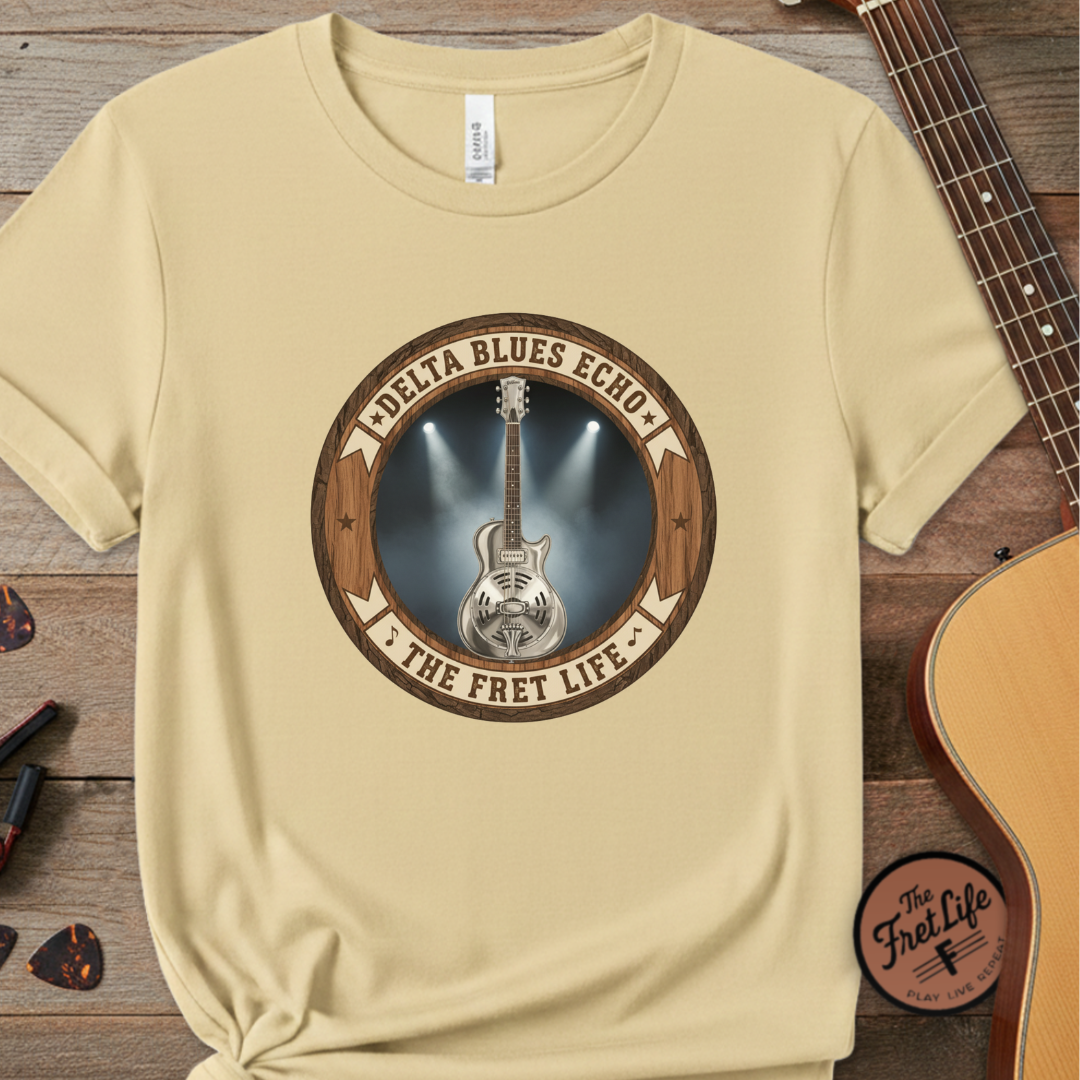 Beige t-shirt with guitar graphic and text on a wooden surface with a guitar.