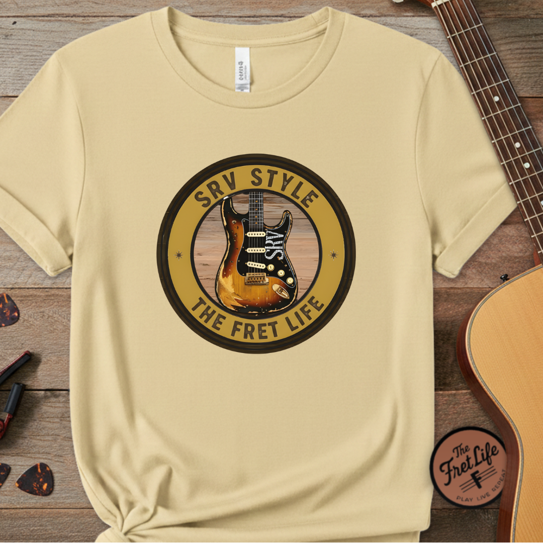 Beige t-shirt with guitar graphic and 'The Fret Life' text on a wooden surface with a guitar.
