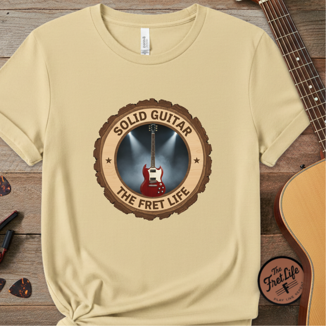 Beige t-shirt with guitar graphic and text on a wooden surface with a guitar.