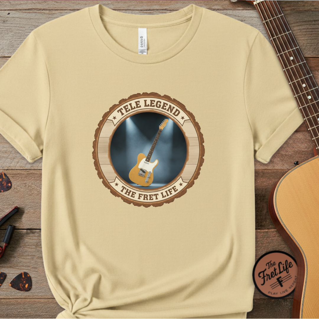 Beige t-shirt with guitar graphic and text on a wooden surface with a guitar and accessories.