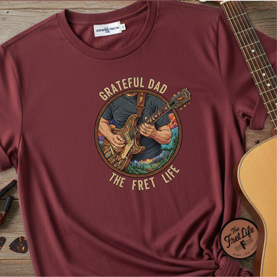 Maroon t-shirt with 'Grateful Dad The Fret Life' graphic and guitar on a wooden surface.