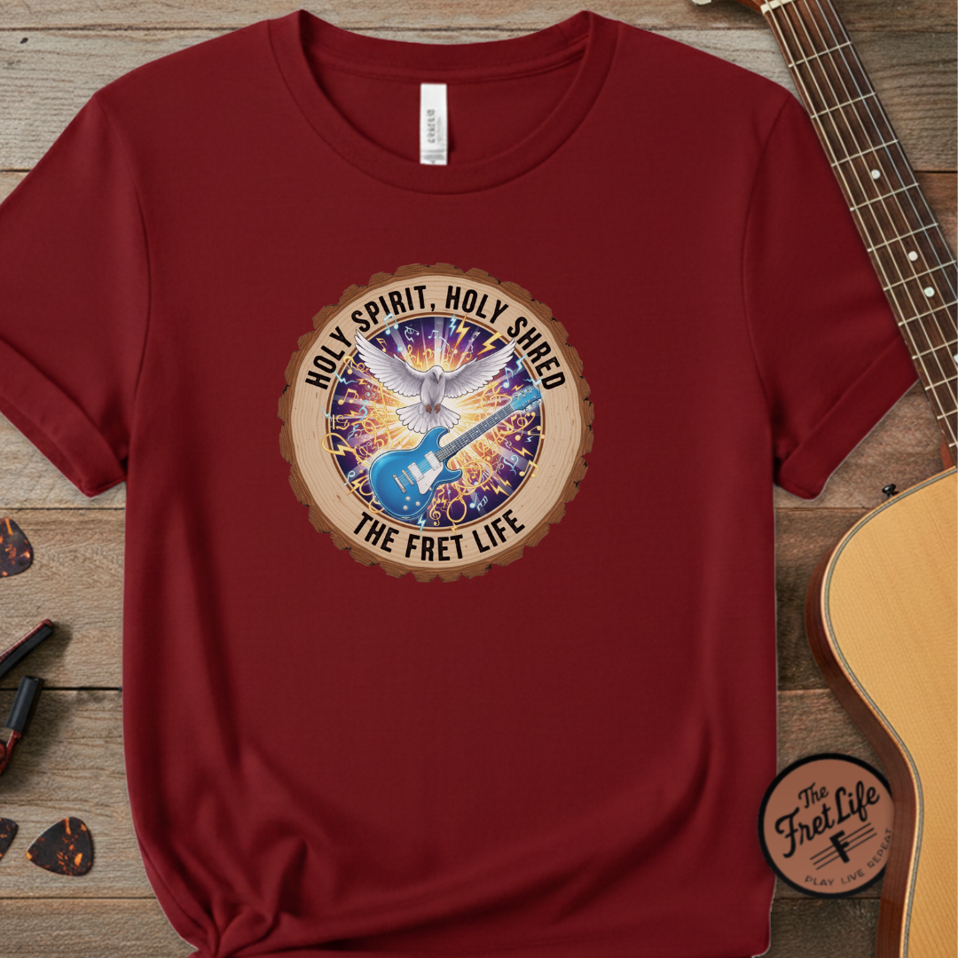 Red t-shirt with a colorful graphic and text on a wooden surface with a guitar.