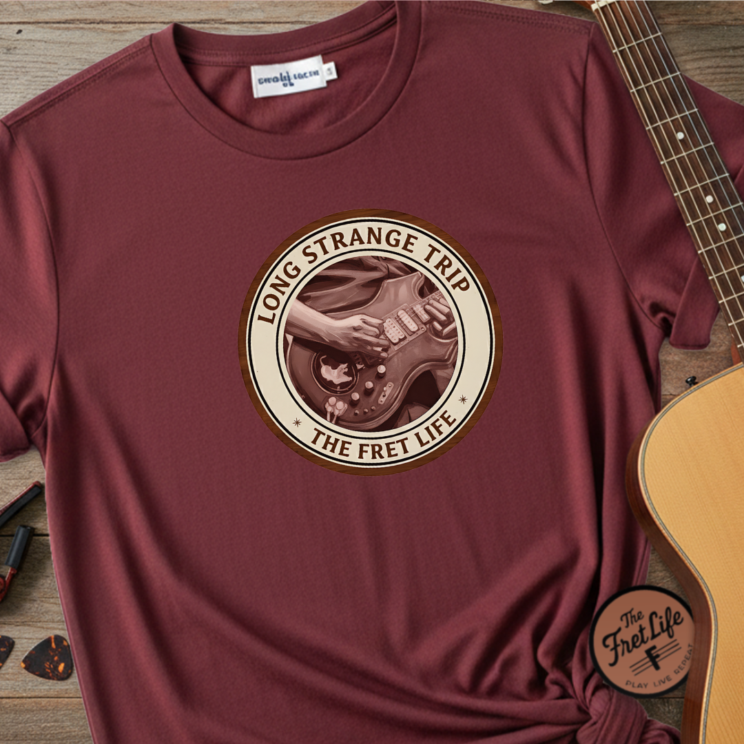 Maroon t-shirt with 'Long Strange Trip: The Fret Life' graphic on a wooden surface with a guitar.