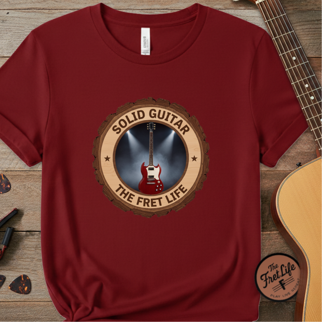 Red t-shirt with 'Solid Guitar The Fret Life' design on a wooden surface with a guitar.