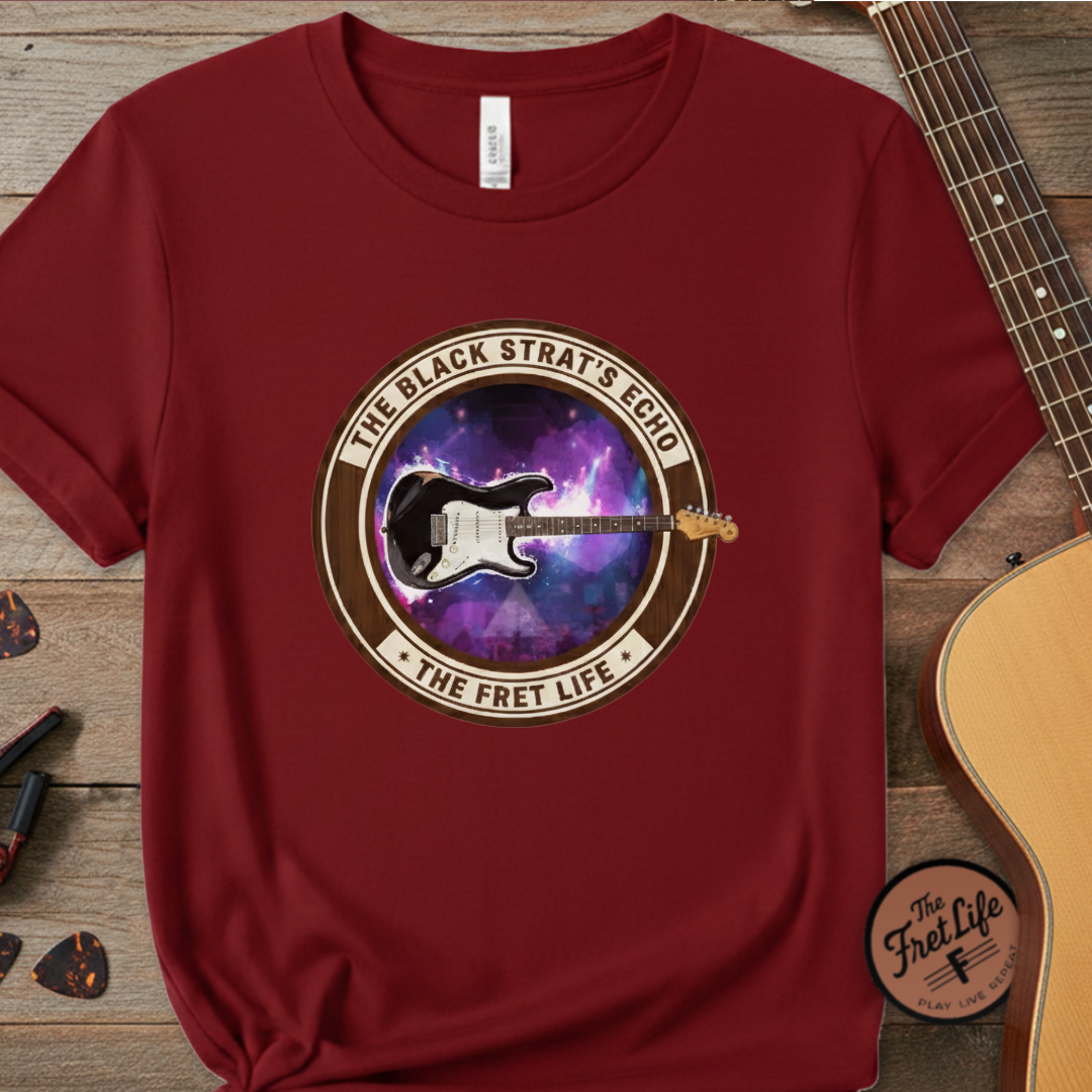 Red t-shirt with guitar graphic and text on a wooden surface with a guitar.