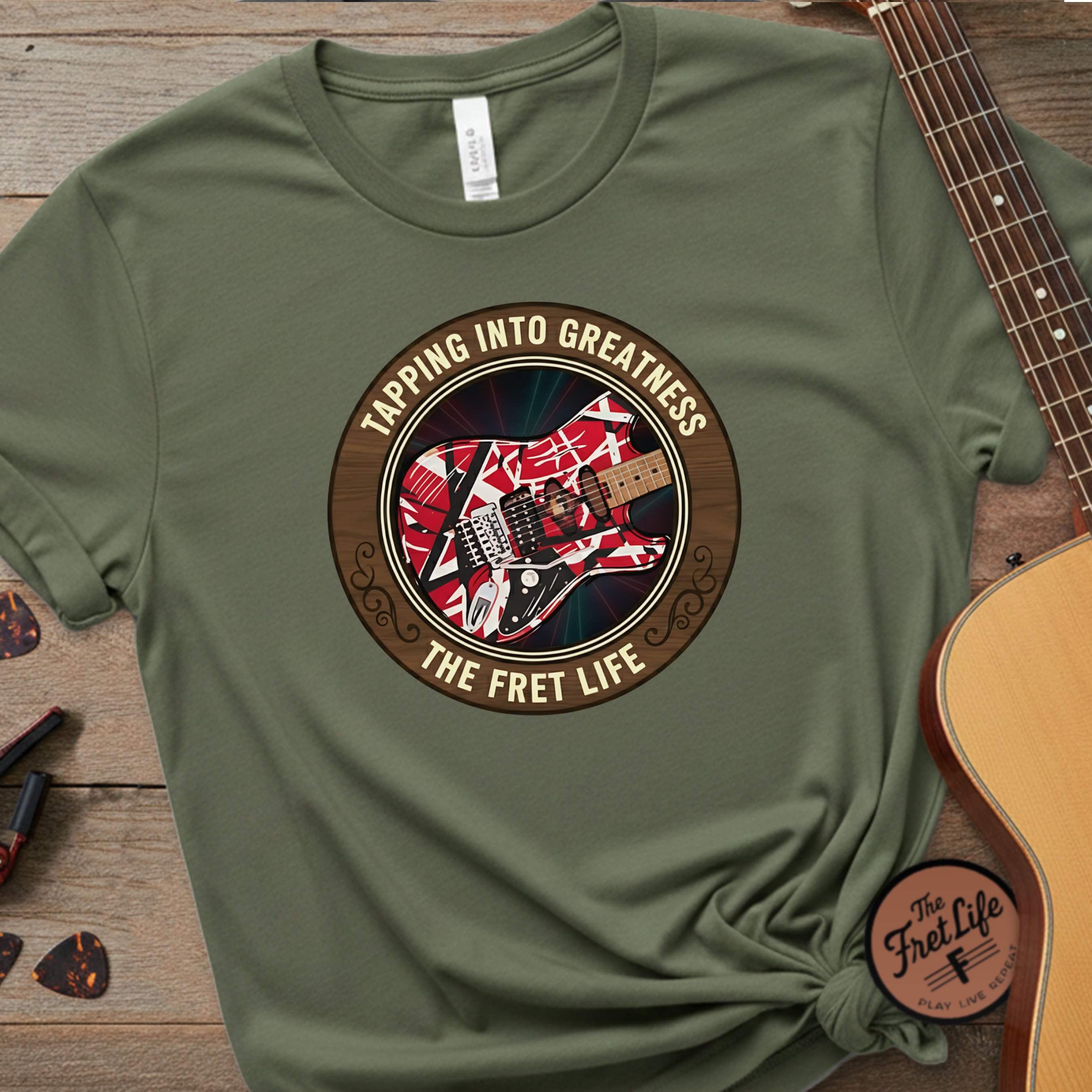Green t-shirt with guitar graphic and text 'Tapping into Greatness, The Fret Life' on a wooden surface with a guitar.