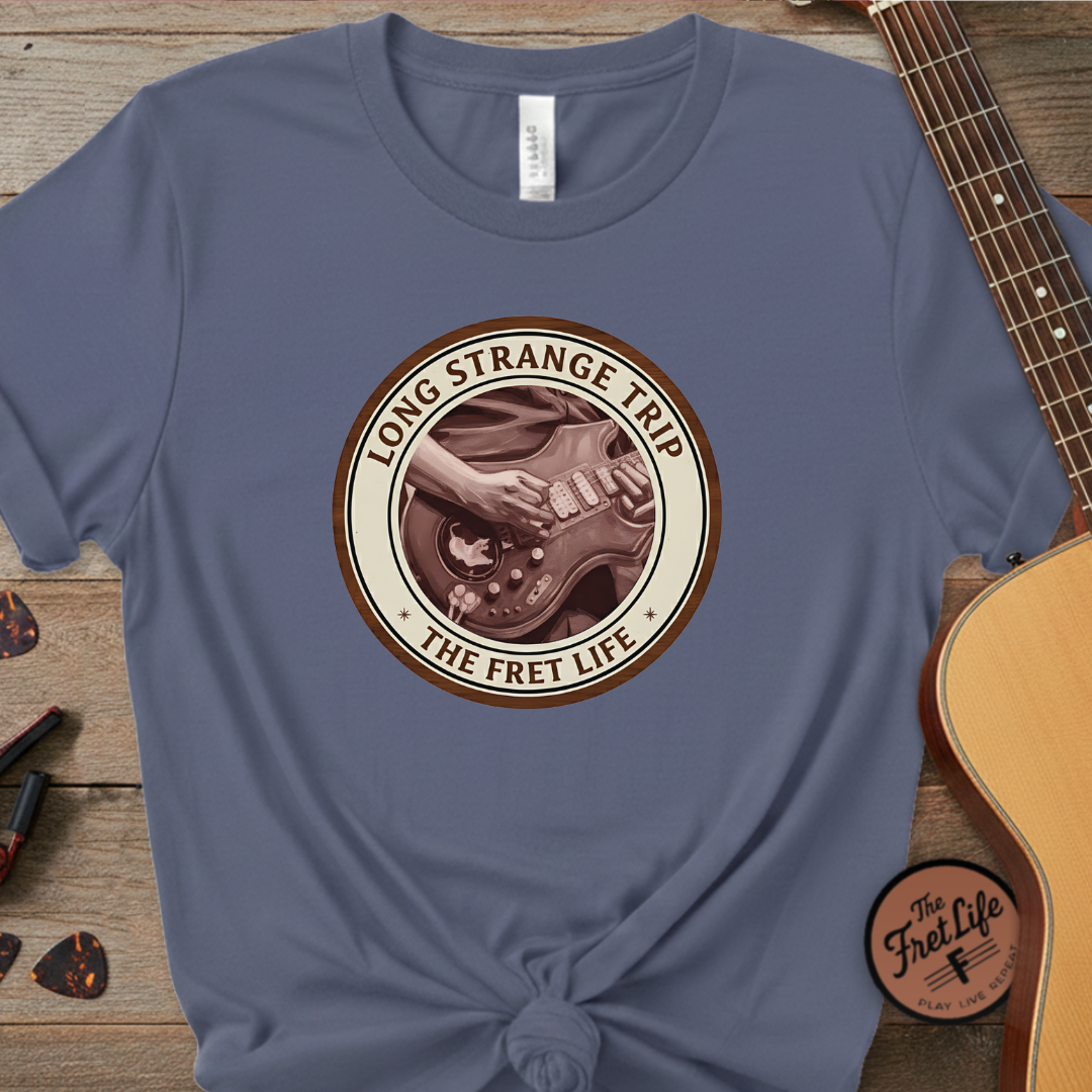 Blue t-shirt with 'Long Strange Trip' graphic on a wooden surface with a guitar