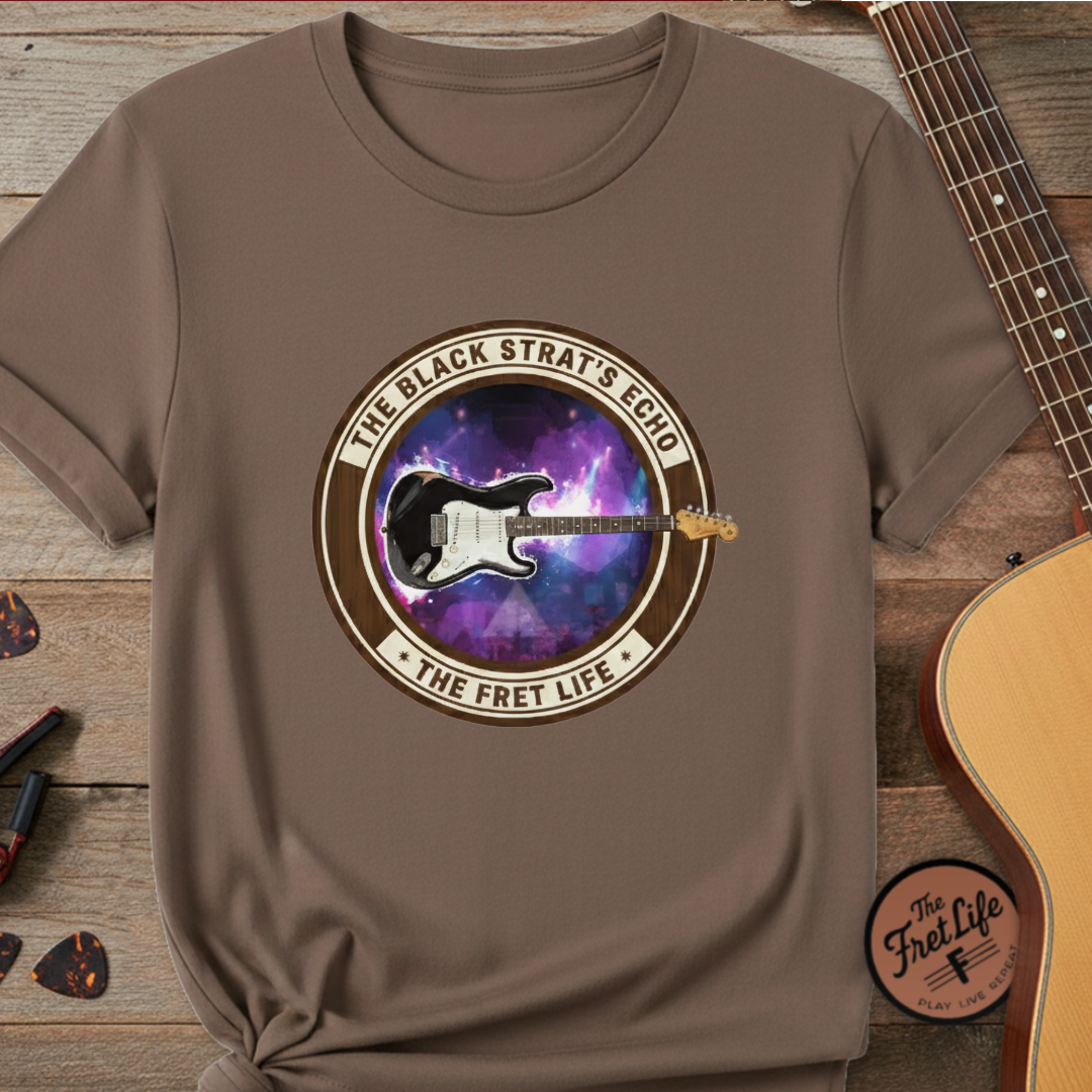 Brown t-shirt with a guitar graphic and text on a wooden surface with a guitar and pick.