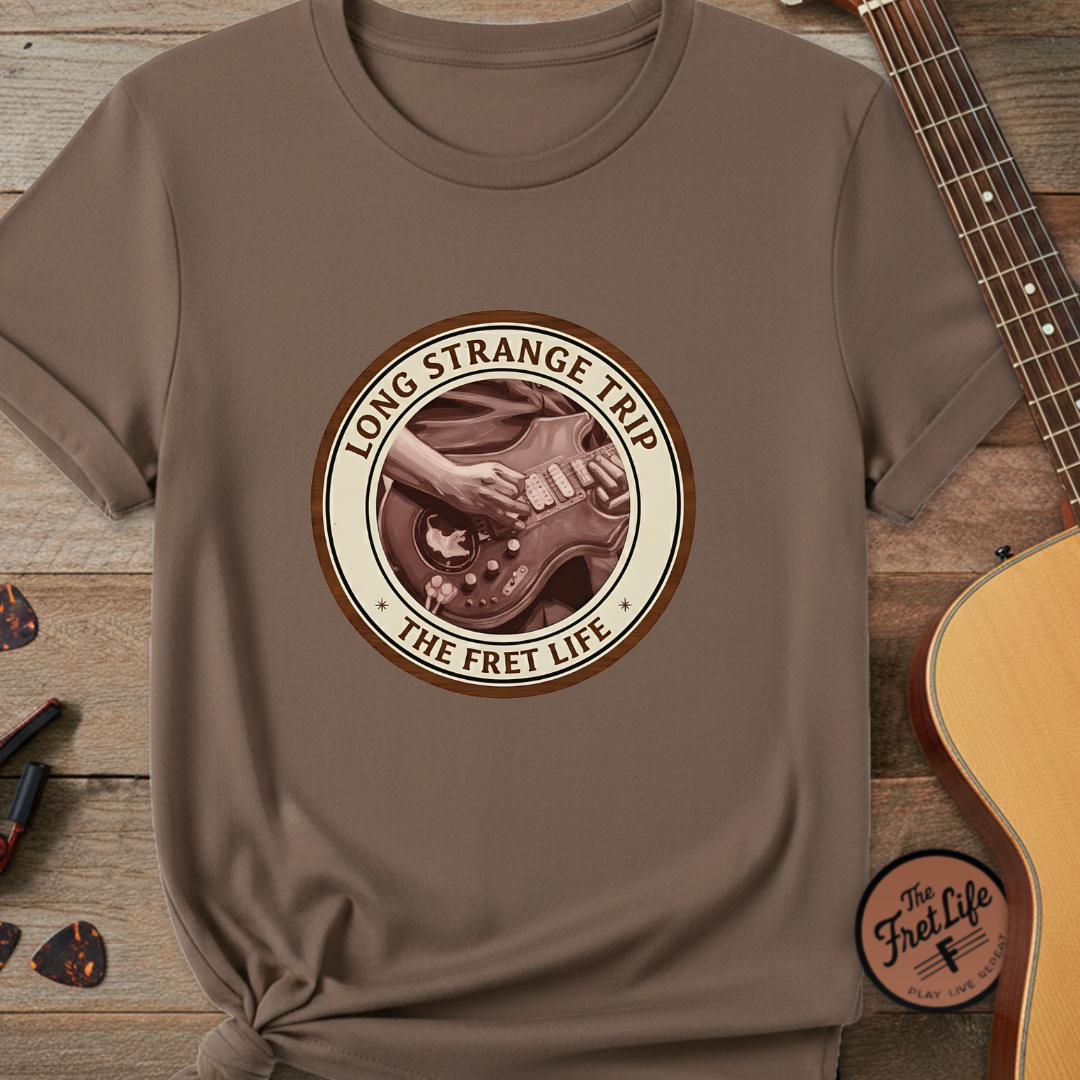 Brown t-shirt with 'Long Strange Trip The Fret Life' design on a wooden surface with a guitar.