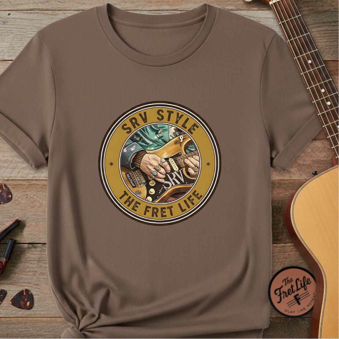 Brown t-shirt with 'SRV Style The Fret Life' graphic on a wooden surface with a guitar.