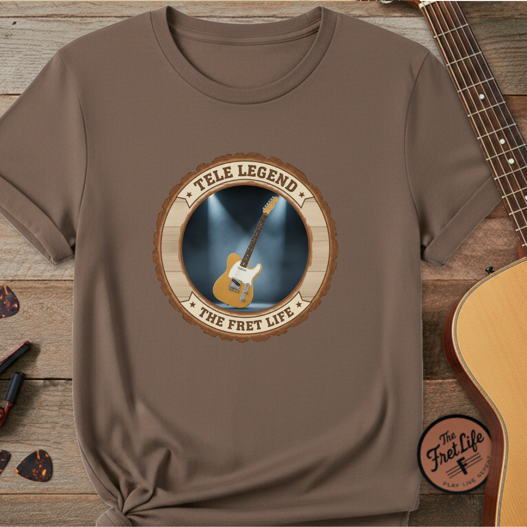 Brown t-shirt with guitar graphic and 'The Fret Life' text on a wooden surface with a guitar.