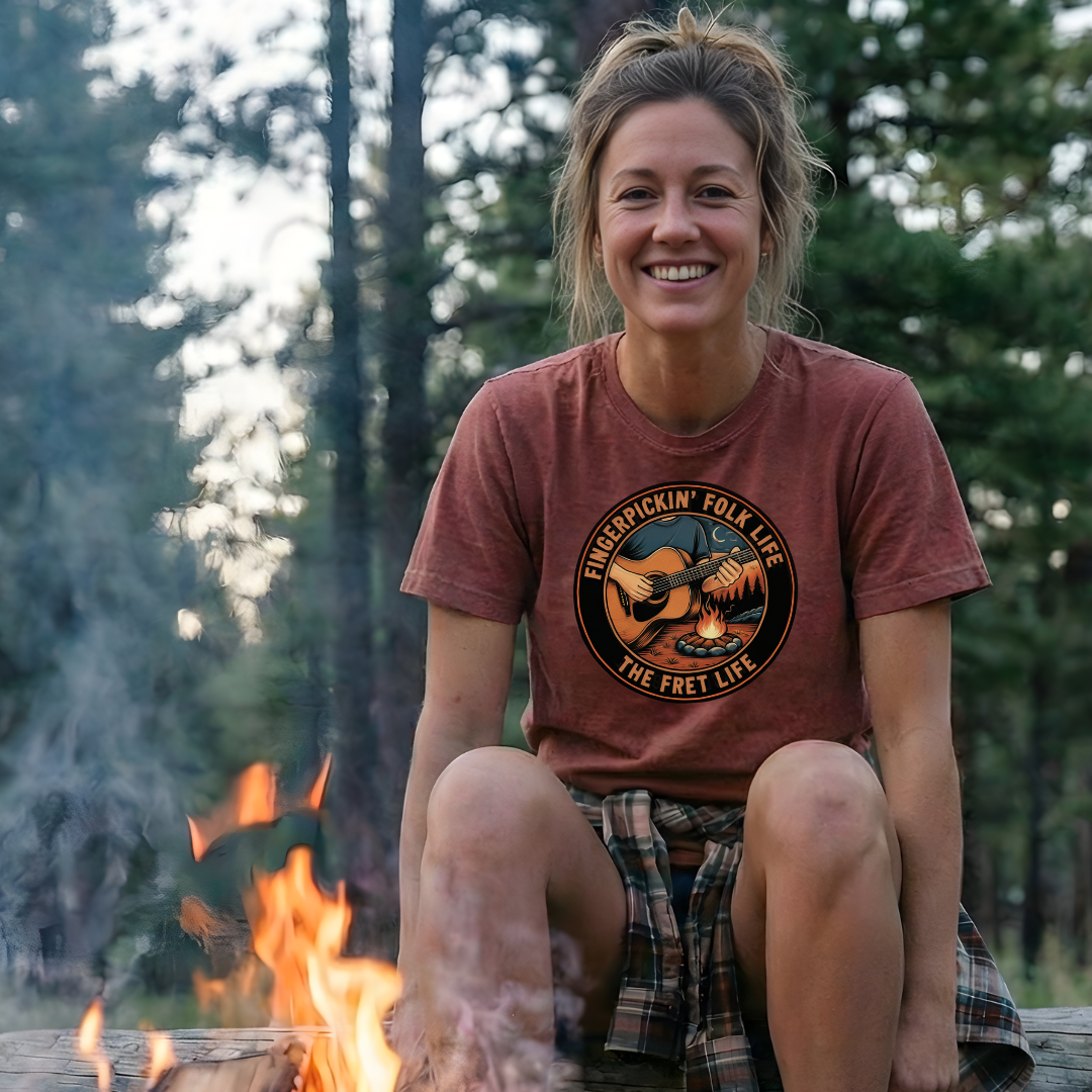 Woman sitting by a campfire wearing a t-shirt with a graphic design in a forest setting