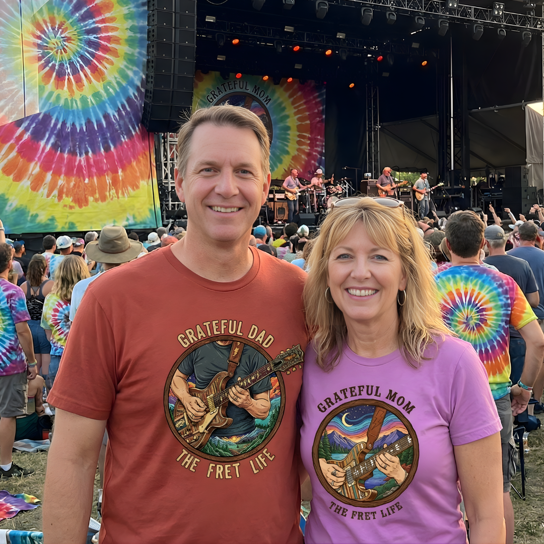 Two people wearing 'Grateful Dad' and 'Grateful Mom' t-shirts at a music festival with tie-dye banners in the background.