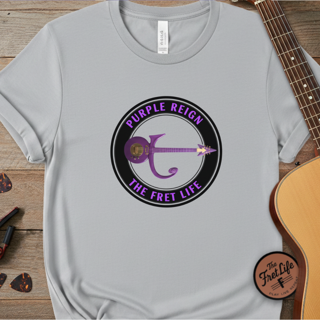 Gray t-shirt with 'Purple Reign The Fret Life' design on a wooden surface with a guitar.