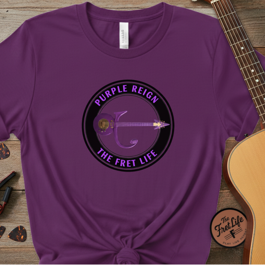 Purple t-shirt with 'Purple Reign The Fret Life' design on a wooden surface with a guitar.