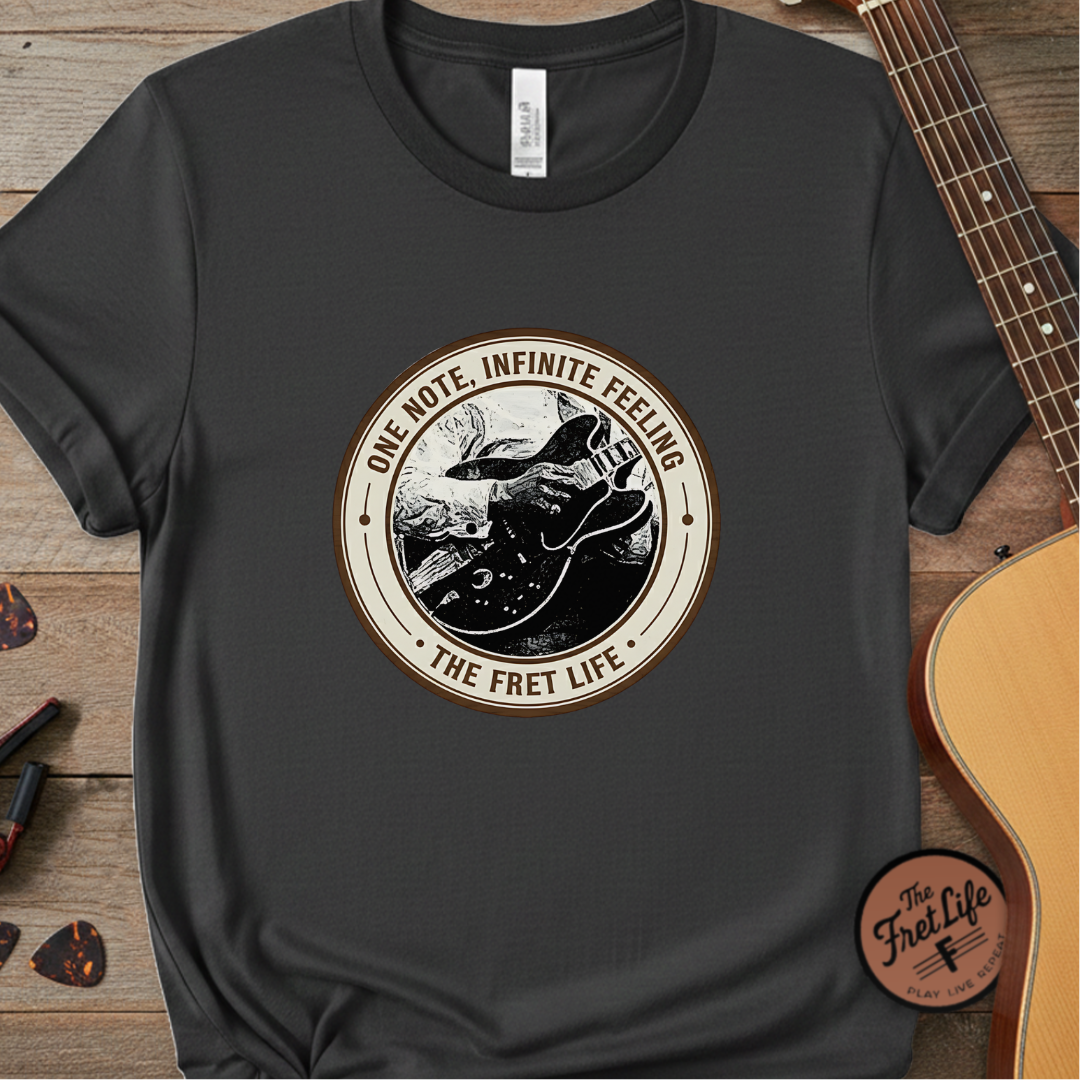 Black t-shirt with 'The Fret Life' graphic design on a wooden surface with a guitar.