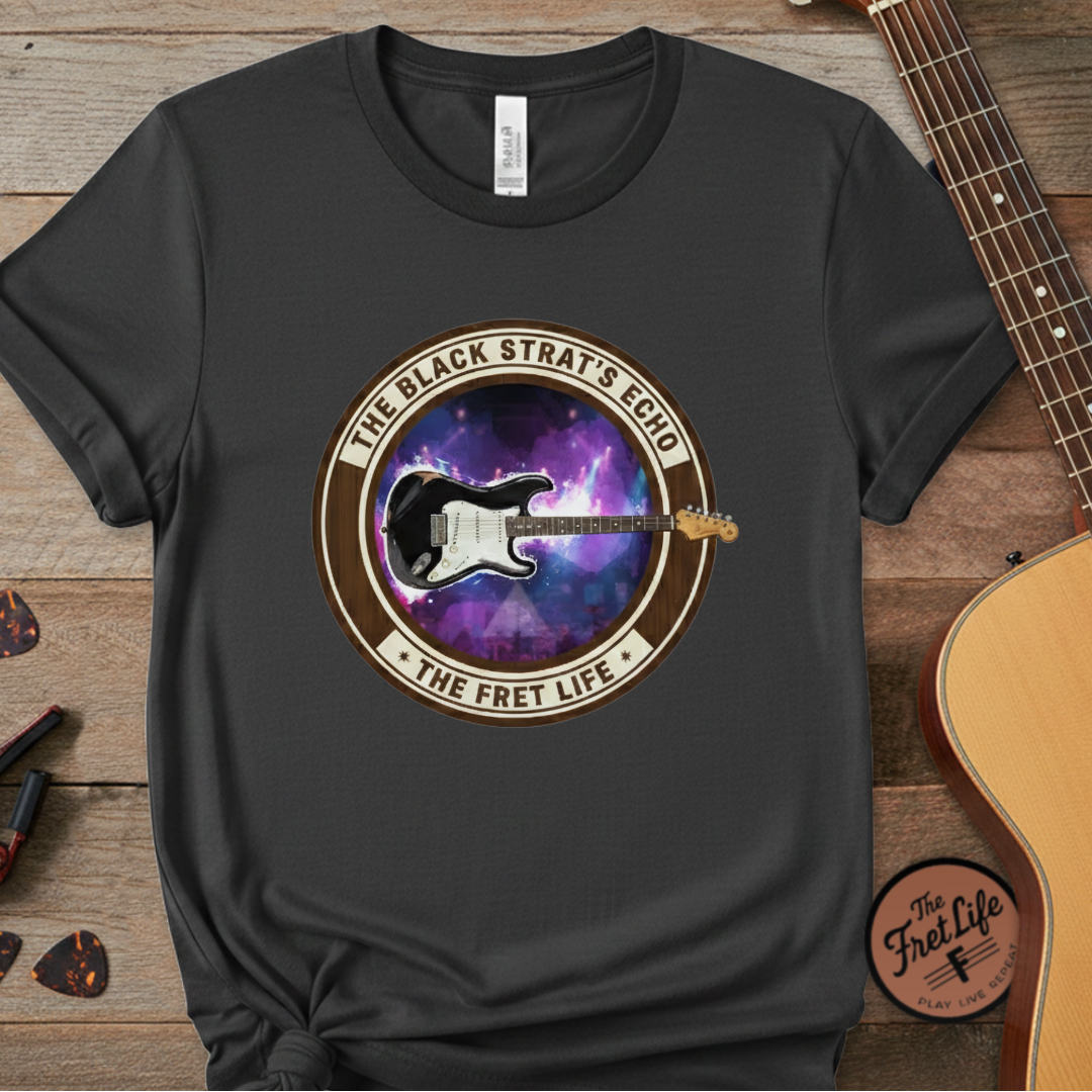 Black t-shirt with guitar graphic and text on a wooden surface with guitars.