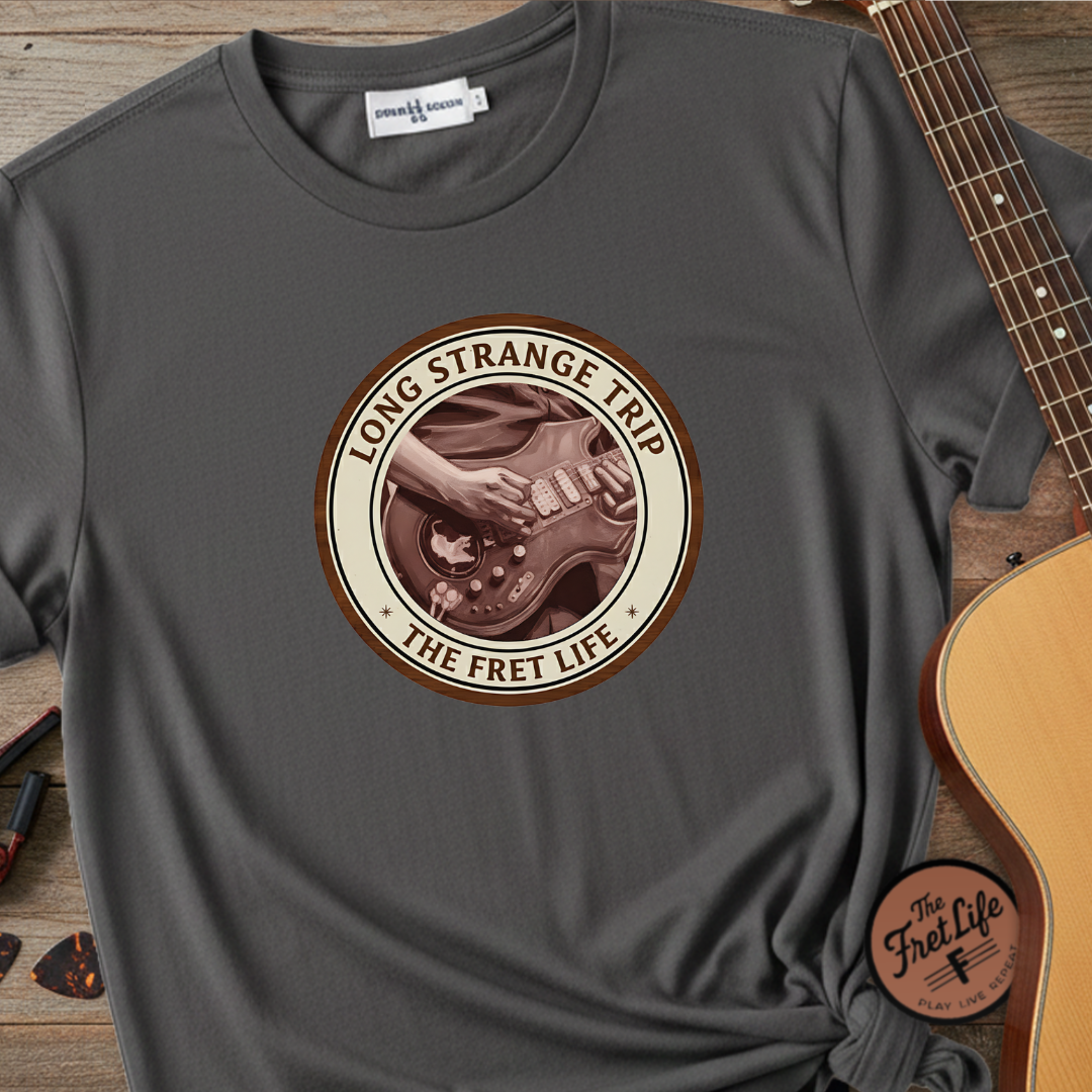 Gray t-shirt with 'Long Strange Trip' graphic design on a wooden surface with a guitar.
