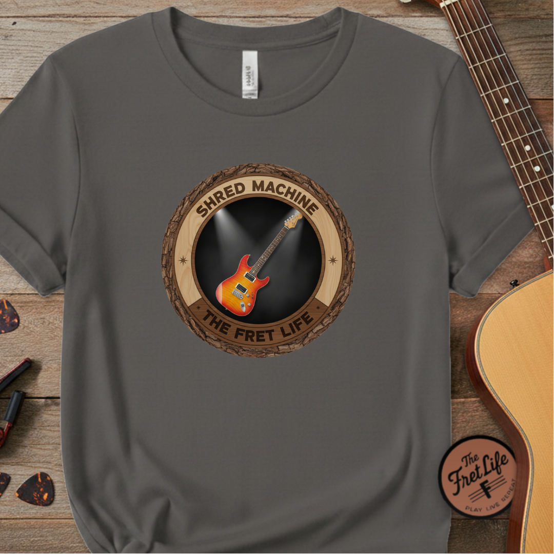 Gray t-shirt with guitar graphic and 'Shred Machine' text on a wooden surface with a guitar.