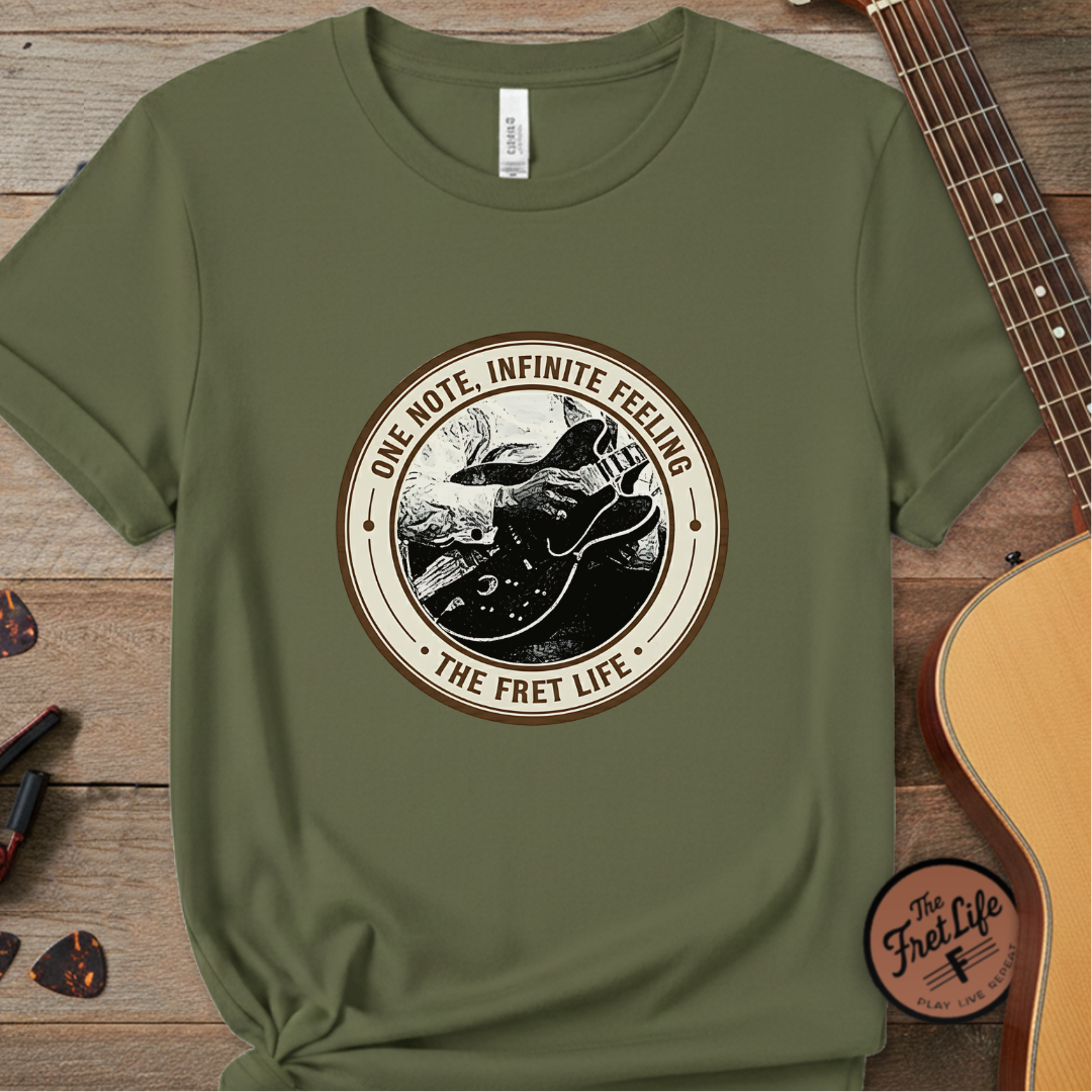 Green t-shirt with 'The Fret Life' graphic on a wooden surface with a guitar.