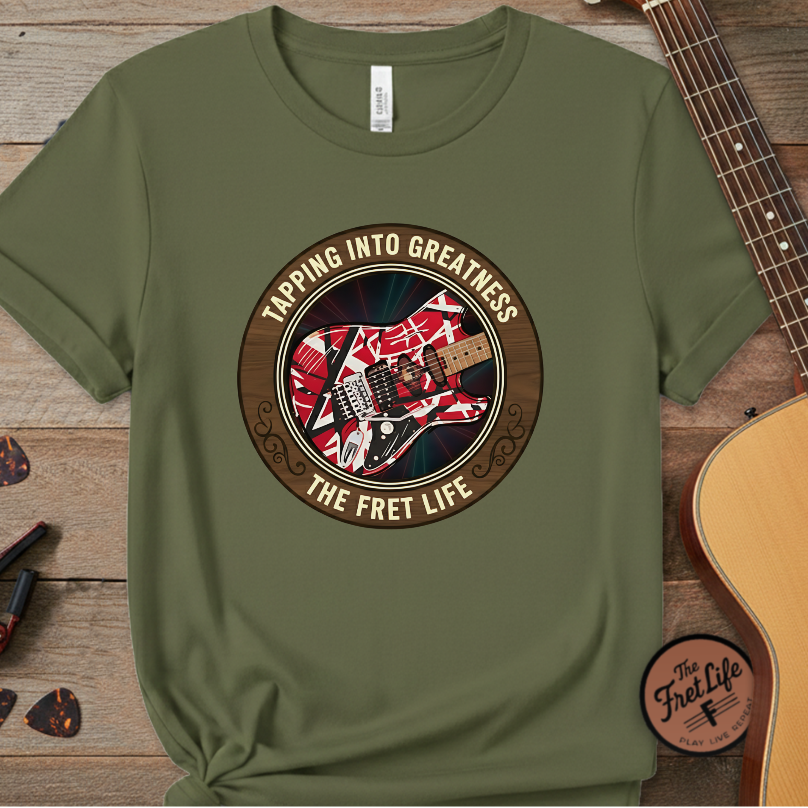 Green t-shirt with guitar graphic and text 'Tapping into Greatness, The Fret Life' on a wooden surface with a guitar.