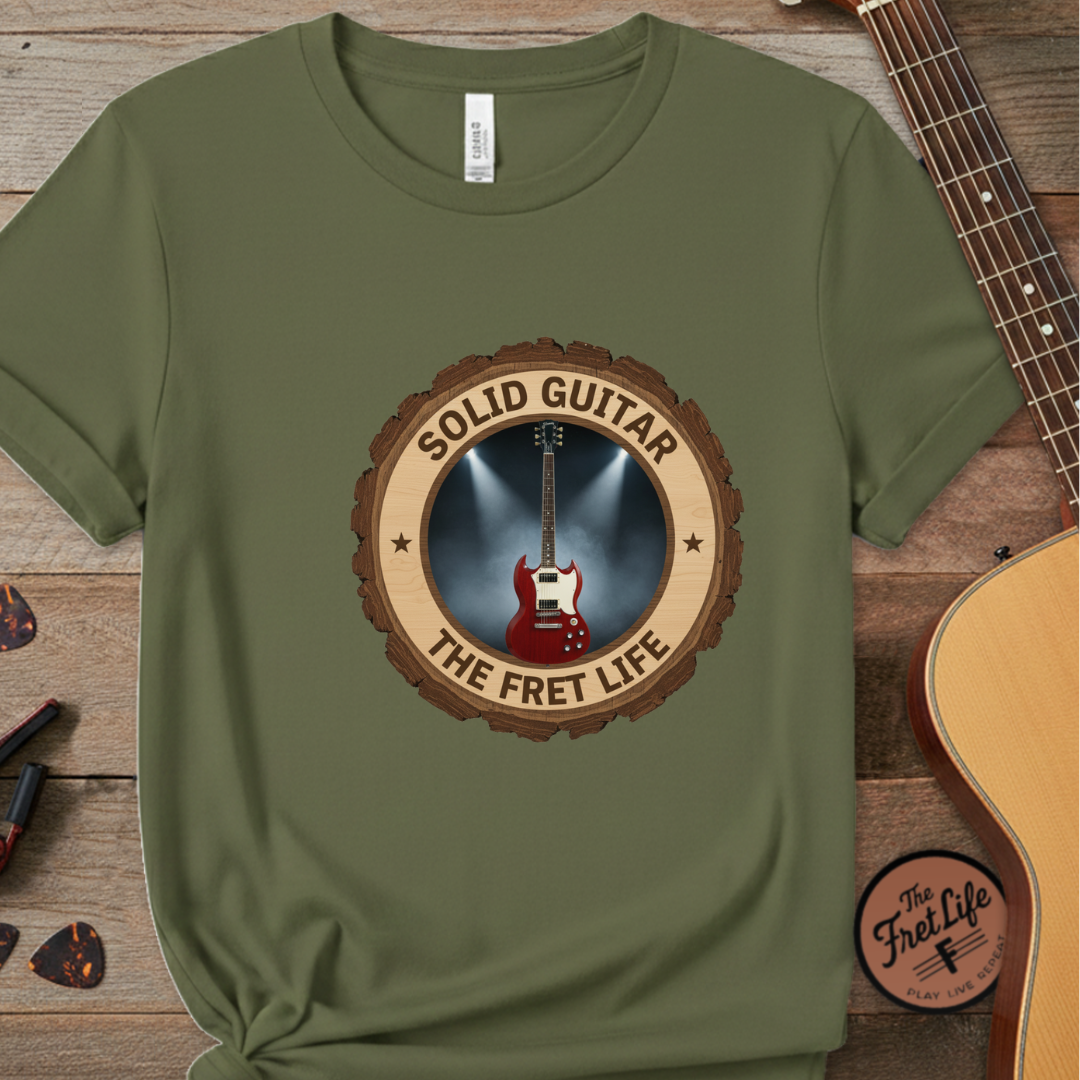 Green t-shirt with 'Solid Guitar The Fret Life' design on a wooden surface with a guitar.